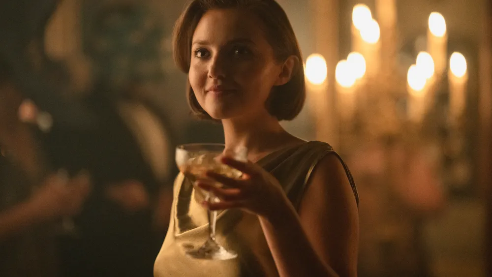"Woman in a gold dress holding a drink at an elegant, dimly lit party with candlelight in the background, creating a warm, sophisticated atmosphere."